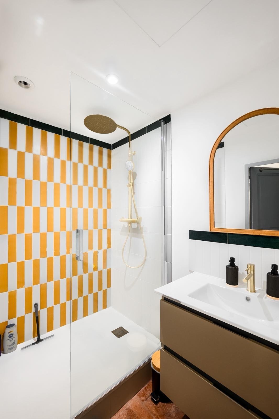 Salle de bain au carrelage damier jaune, douche à l'italienne dorée et miroir arche