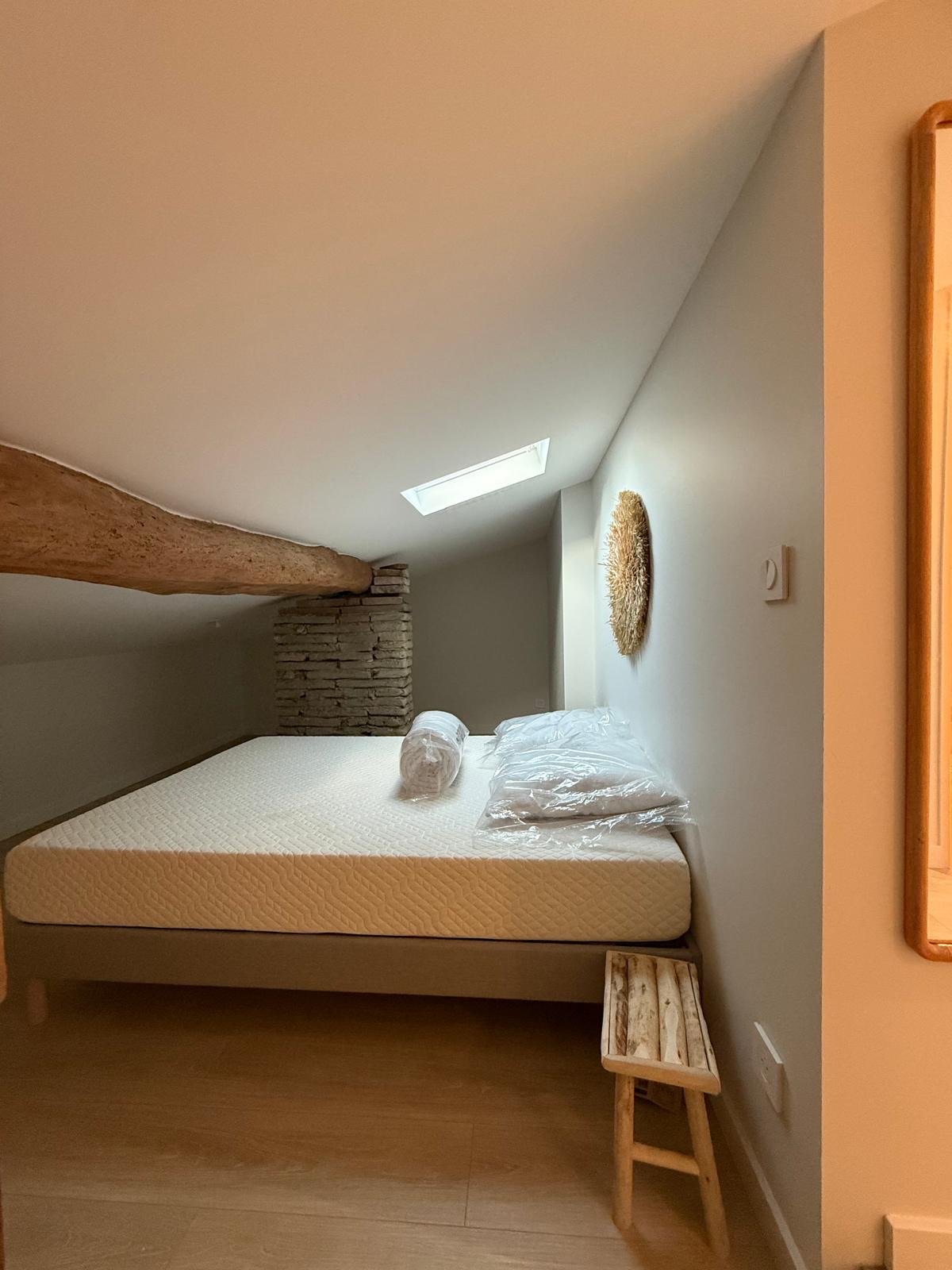 Chambre sous combles avec lit, fenêtre de toit et poutre